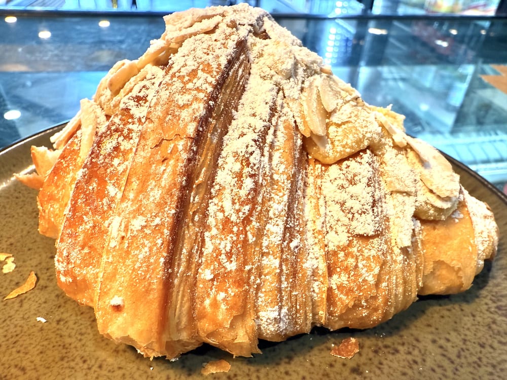 Almond croissant topped with sliced almonds and powdered sugar