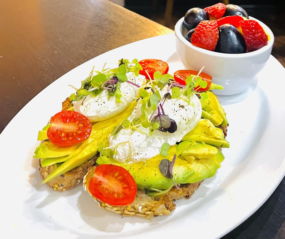 Avocado toast topped with poached eggs and a side of fruit