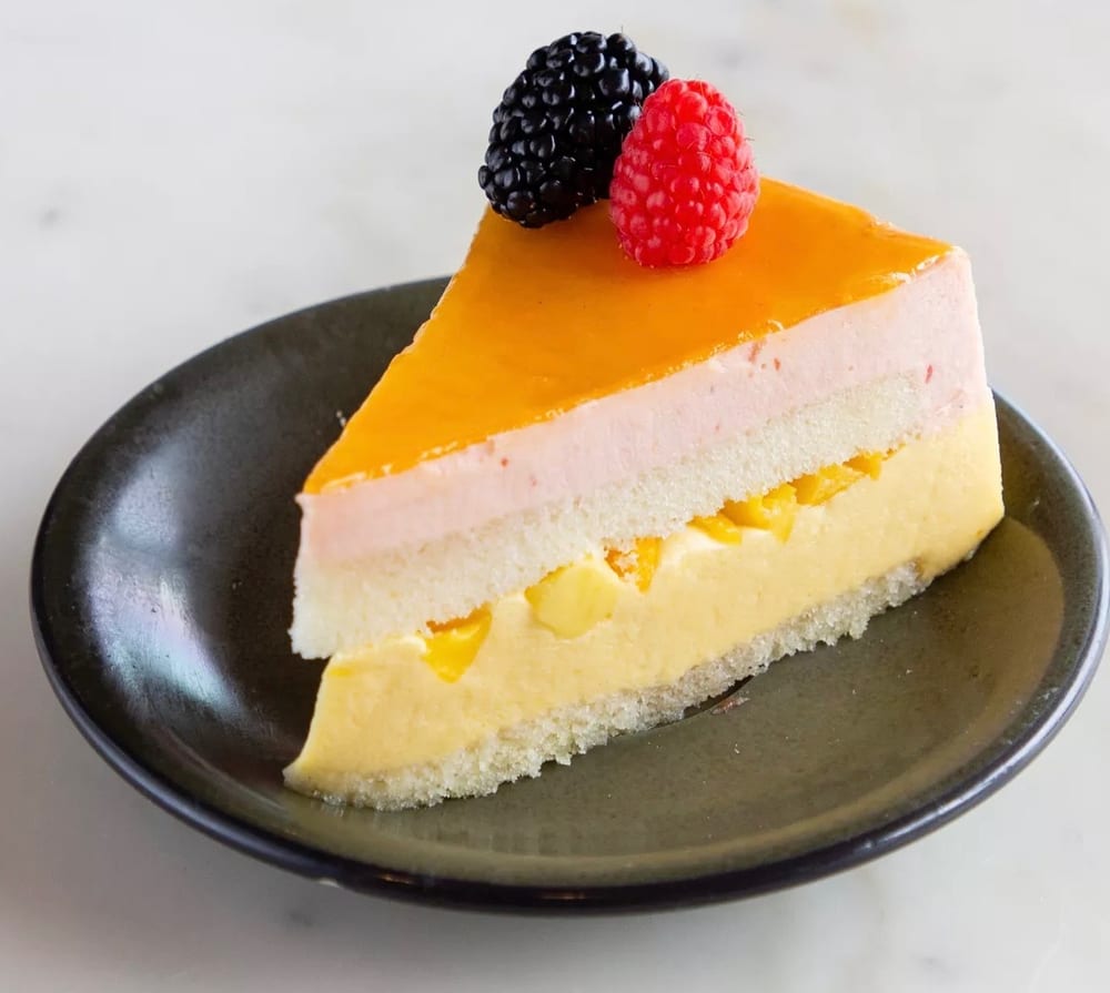 Slice of mango mousse cake topped with berries